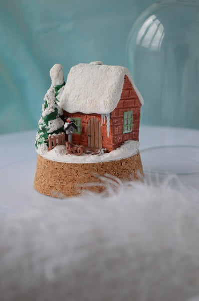 Small model of a snowy cabin with a tree on a cork base.