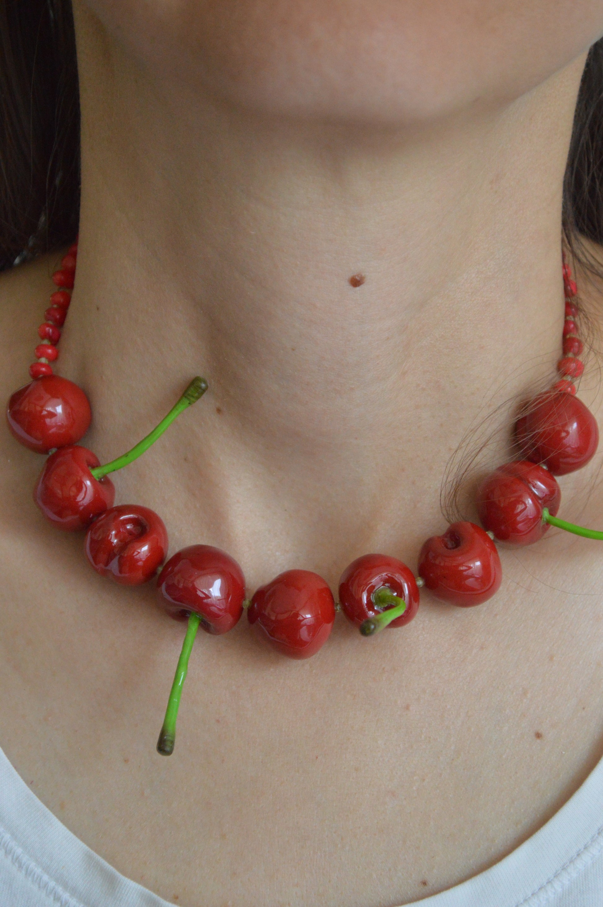 Necklace made of red cherries with green stems around a person's neck.
