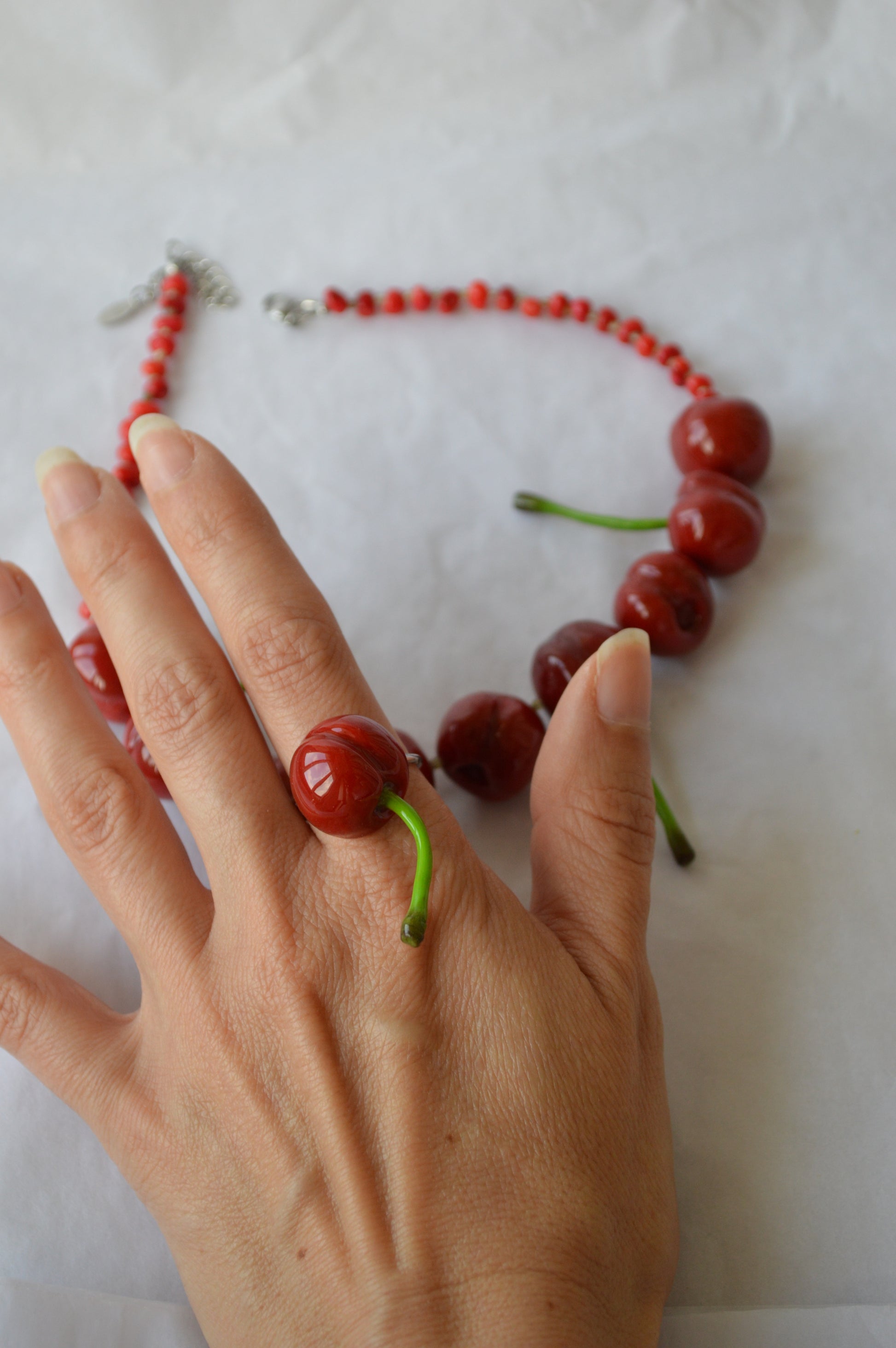 Hand wearing a ring made of cherries with a necklace of cherries on a white background