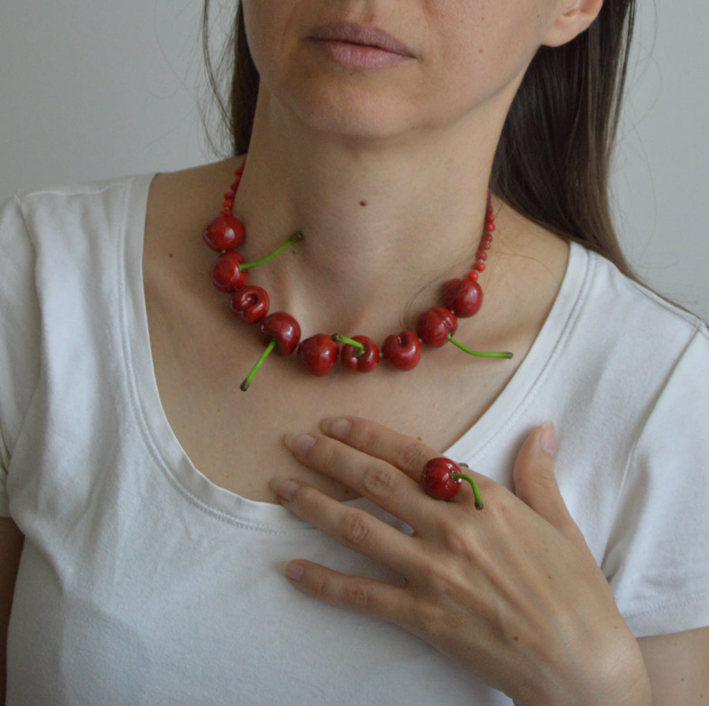 Person wearing a necklace made of red berries and green stems, holding a single berry.