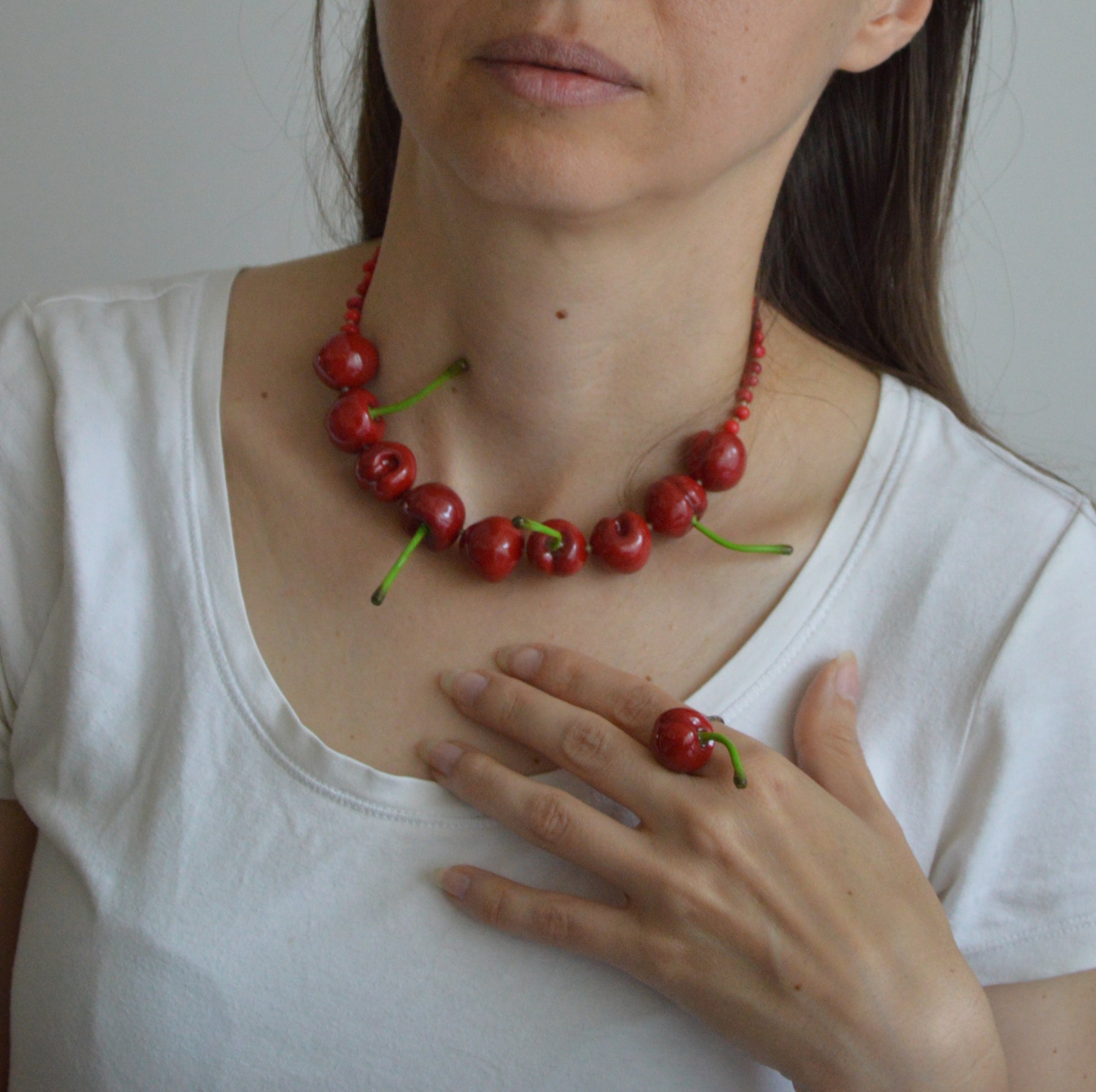 Person wearing a necklace made of red berries and green stems, holding a single berry.