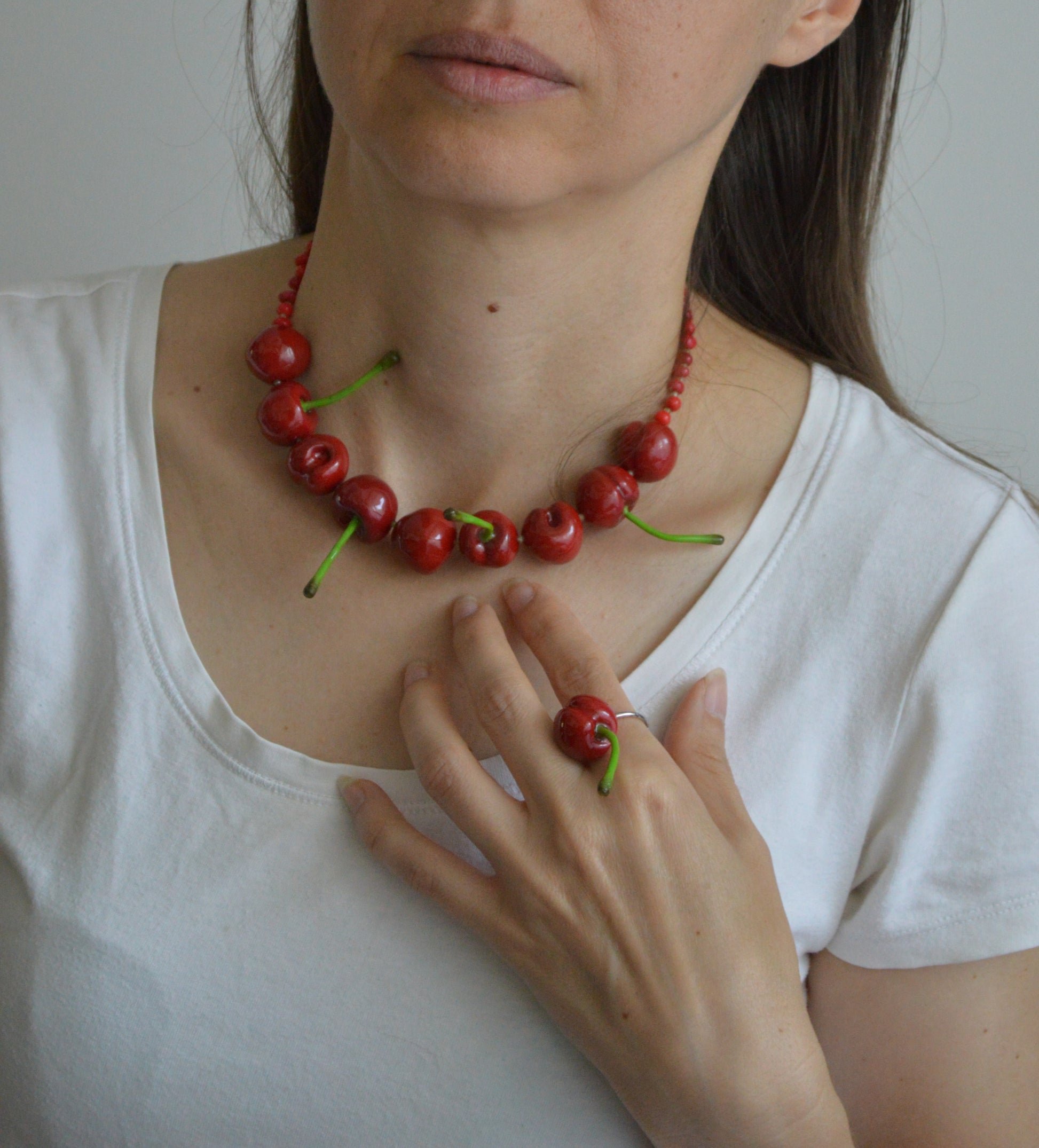 Person wearing a red berry necklace and ring on a plain background