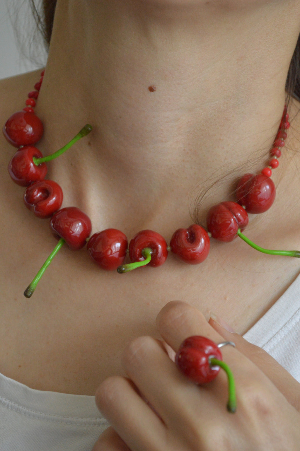 Person wearing a necklace and ring made of red cherries with green stems.