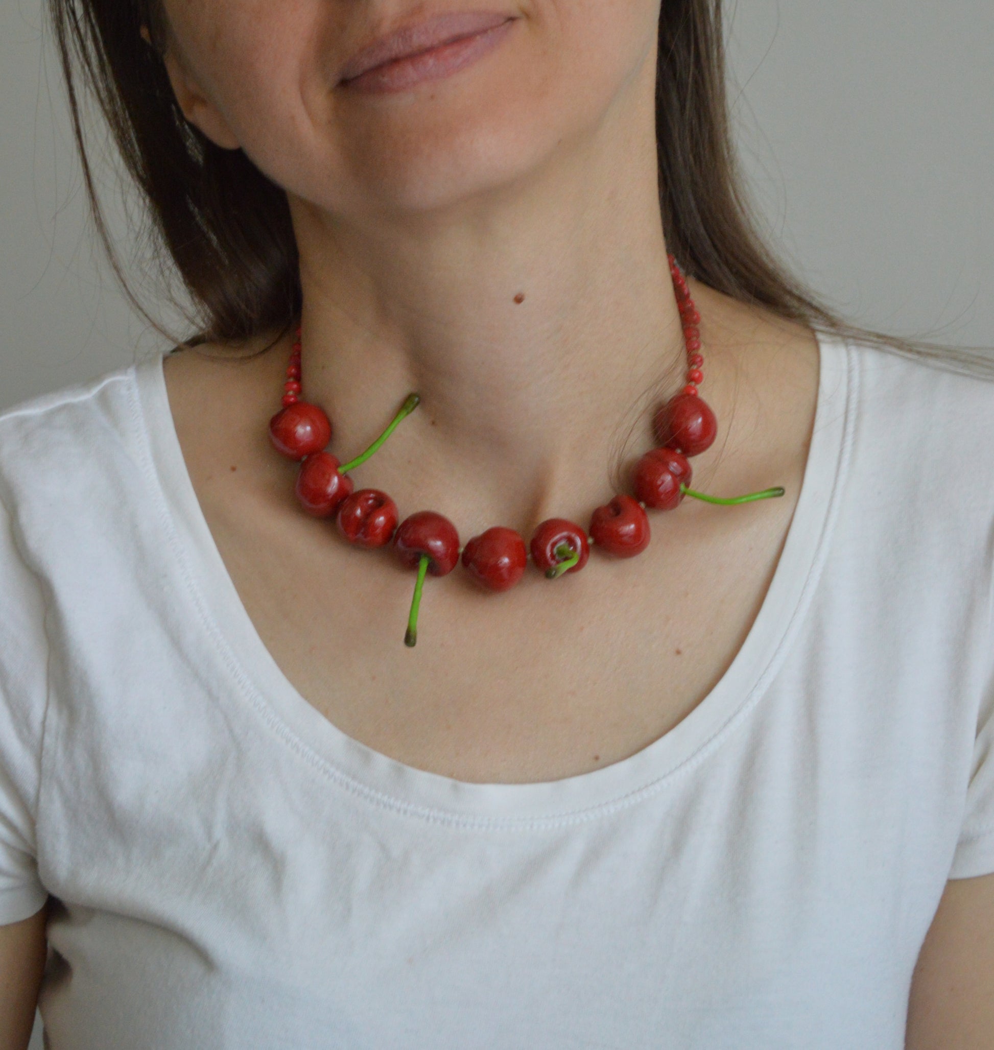 Person wearing a necklace made of red berries and green stems against a neutral background