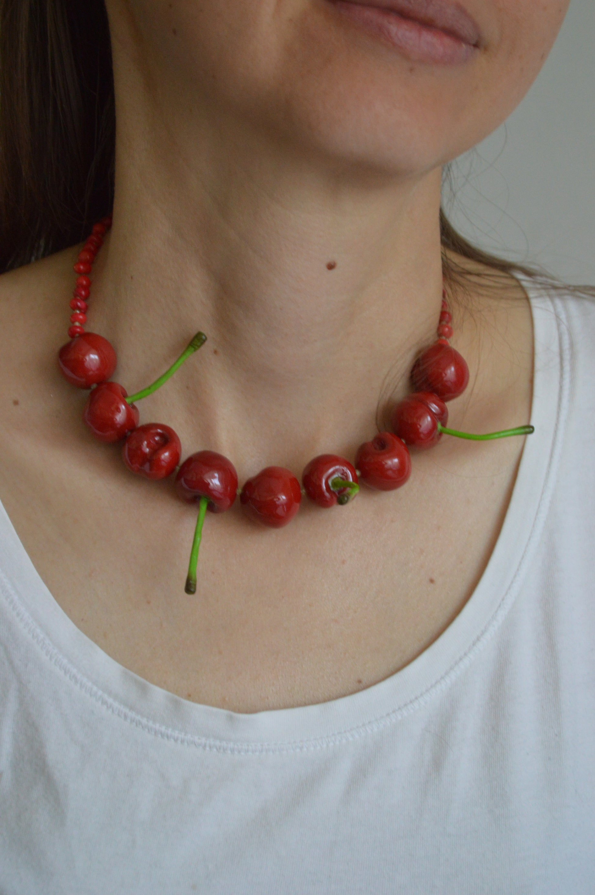 Necklace made of red berries worn by a person in a white tank top.