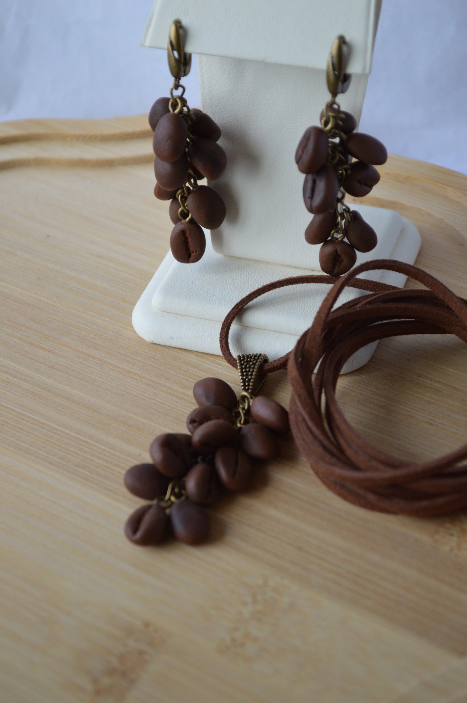 Brown leather cord earrings with coffee bean-like beads on a white stand.