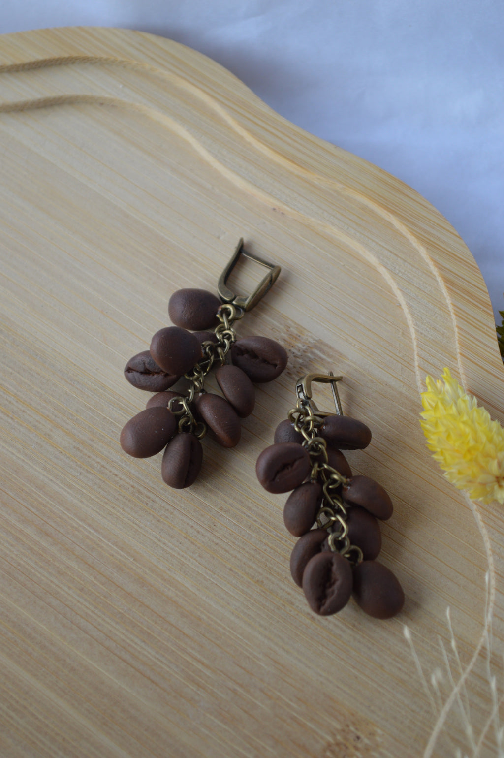 Brown beaded earrings on a wooden surface with a yellow flower in the background