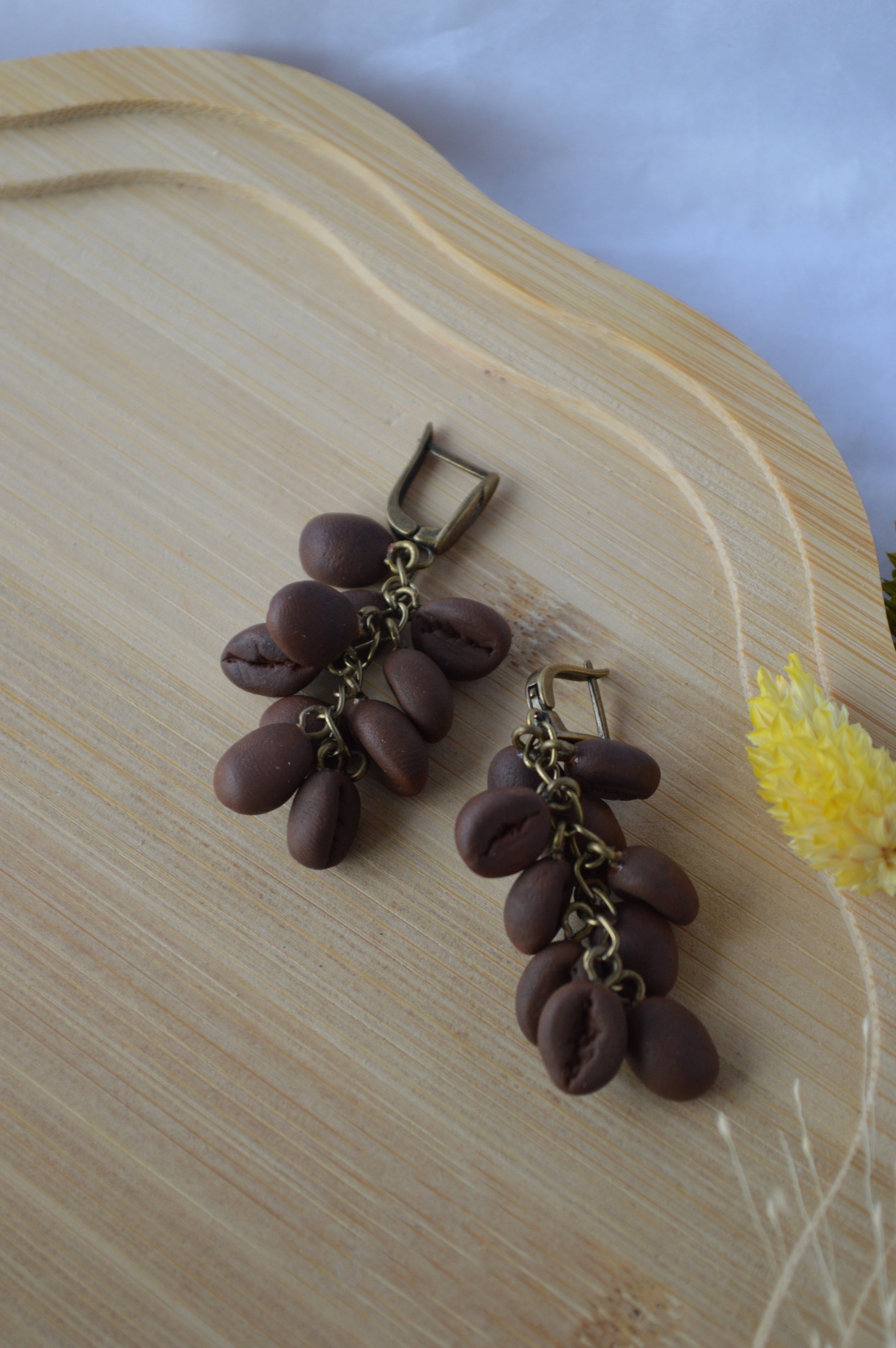 Brown beaded earrings on a wooden surface with a yellow flower in the background