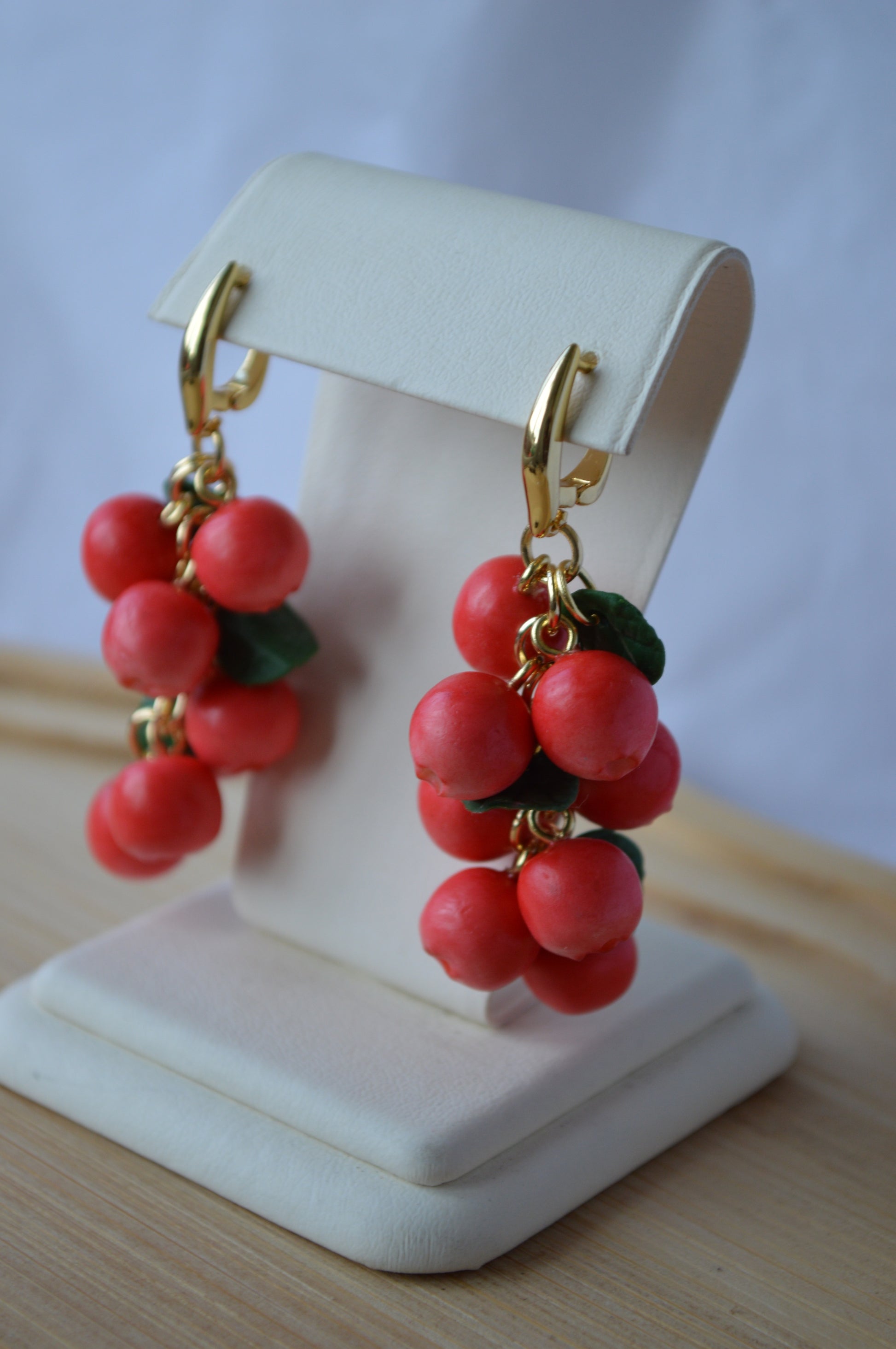 Red berry earrings on a white stand with a light background
