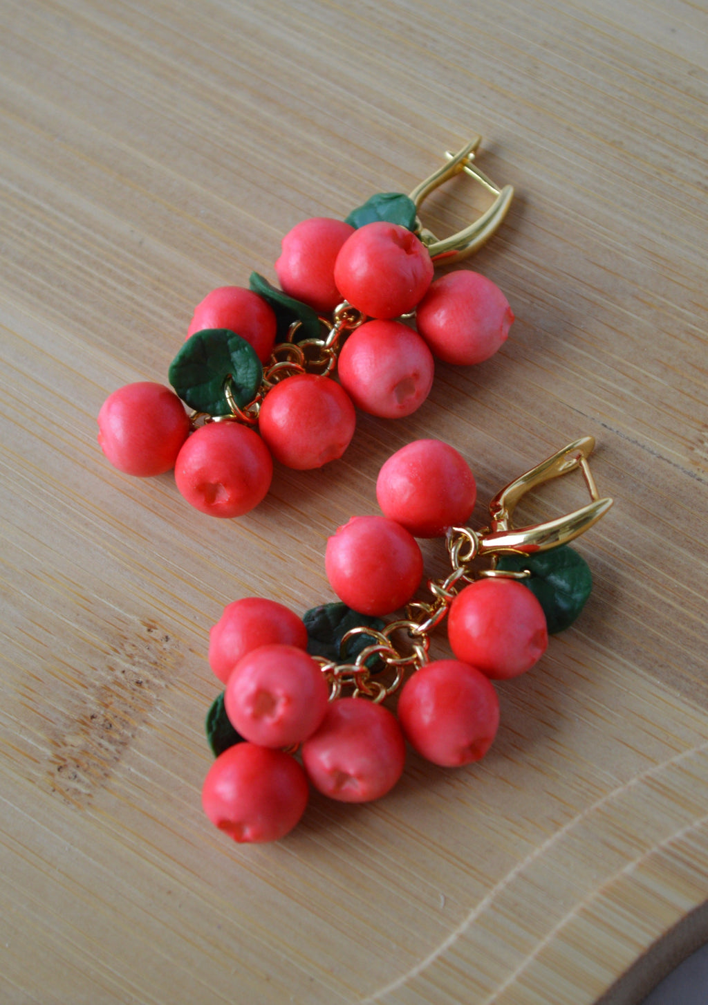 Pair of earrings with red berry-like beads and gold accents on a wooden surface