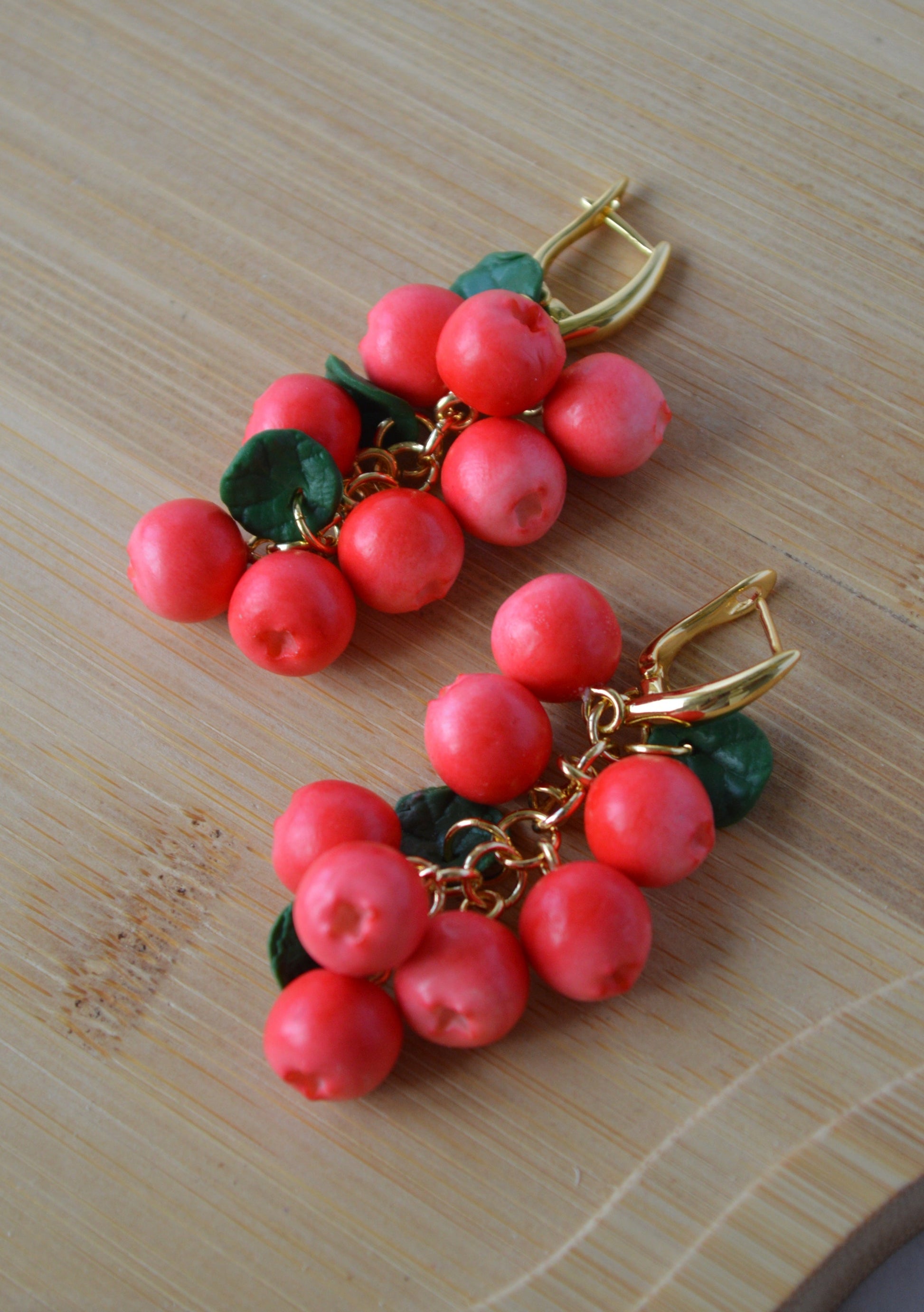 Pair of earrings with red berry-like beads and gold accents on a wooden surface